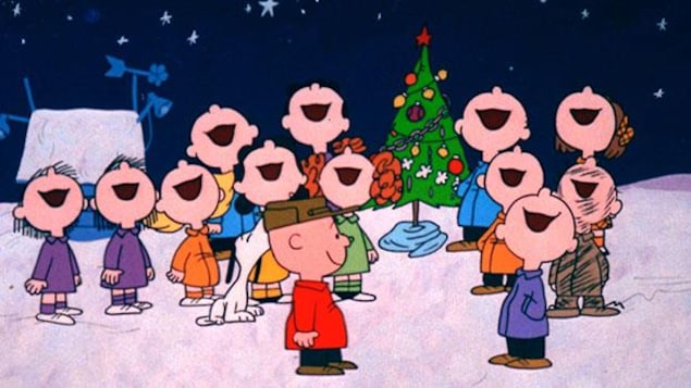 Charlie Brown sourit en regardant une chorale d'enfants chanter sous la neige.