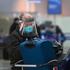 Un voyageur portant un masque et une visière enregistre ses valises à l'aéroport Pearson.