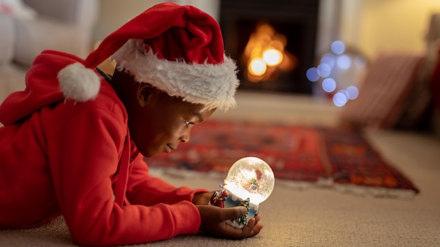 Un garçon avec une tuque de Noël observe une boule à neige.