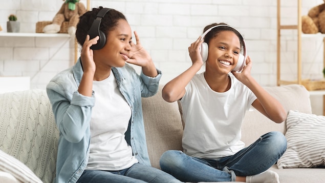 Deux jeunes filles sont sur le divan avec une paire d'écouteur sur les oreilles.