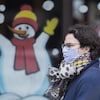 Une femme masquée passe devant une vitrine colorée arborant un dessin de bonhomme de neige.