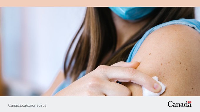 A woman wearing a mask holds a cotton ball on her arm after vaccination. 