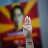 Une main avec trois doigts levés en signe de résistance devant une pancarte à l’effigie de l'ex-cheffe du gouvernement Aung San Suu Kyi.