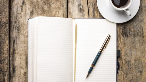Un carnet d'écriture, un stylo et une tasse de café posés sur une table en bois.