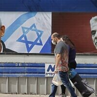People walk past an electoral billboard for the Likud party bearing a portrait of its leader Prime Minister Benjamin Netanyahu (L), and opposition Yesh Atid party leader Yair Lapid, in Tel Aviv, on March 12, 2021, ahead of the March 23 general election. (JACK GUEZ / AFP)