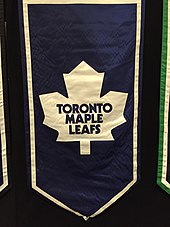 A banner featuring an old Maple Leaf logo, featuring an eleven pointed white maple leaf on a blue background.