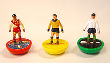 Photo serrée de trois mini-figurines représentant des footballeurs du jeu Subbuteo, une rouge, une jaune et un vert.