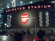 Photo de l'entrée du stade de nuit avec « Emirates Stadium » en majuscules éclairées sur la façade.