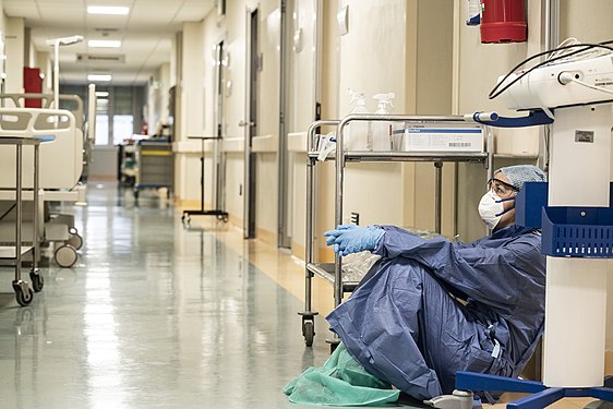 Une femme masquée, assise à même le sol dans un couloir d'hôpital.