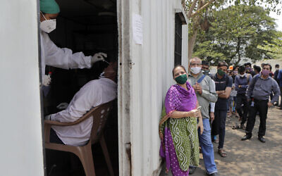 A health worker takes a nasal swab sample of a person to test for COVID-19 as others wait for their turn outside a field hospital in Mumbai, India, Thursday, May 6, 2021. Infections in India hit another grim daily record on Thursday as demand for medical oxygen jumped seven-fold and the government denied reports that it was slow in distributing life-saving supplies from abroad. (AP Photo/Rajanish kakade)