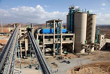 vue d'une usine avec deux convoyeurs au premier plan, un bâitment de type industriel et quatre silos à leur droite
