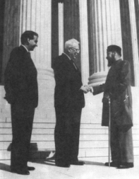 Earl Warren and Maulvi Tamizuddin Khan shake hands as a third man looks on