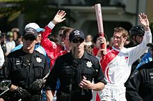 Torchbearer Trevor Robinson carrying the Olympic Torch near Golden Gate Park with the Flame Attendants in blue and SFPD in black.jpg