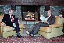 Ronald Reagan and Mikhail Gorbachev sit in plush chairs in front of a stone fireplace