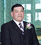 "A colour picture of Tony Whitford, Commissioner of the Northwest Territories during his swearing in ceremony. He is in a dark suit and white shirt with a tie and a flower in the buttonhole."