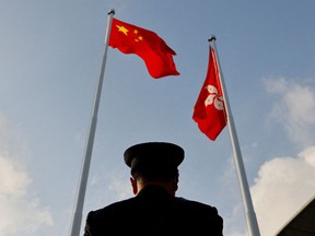 A police officer stands guard below China and Hong Kong flags during a flag raising ceremony, a week ahead of the Legislative Council election in Hong Kong, China, December 12, 2021.