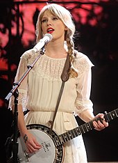 Swift singing into a mic while playing a banjo