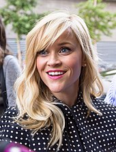 A portrait of a Reese Witherspoon, a blonde white woman. She is wearing a polka dot shirt and pink lipstick.