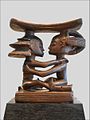 sculpture monoxyle avec une partie supérieure formant un croissant arrondi porté par deux personnages assis se faisant face