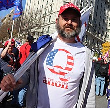 Man wearing a t-shirt with a design consisting of block letter "Q" overlaid with an American flag pattern