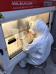 A seated laboratory worker in protective clothing