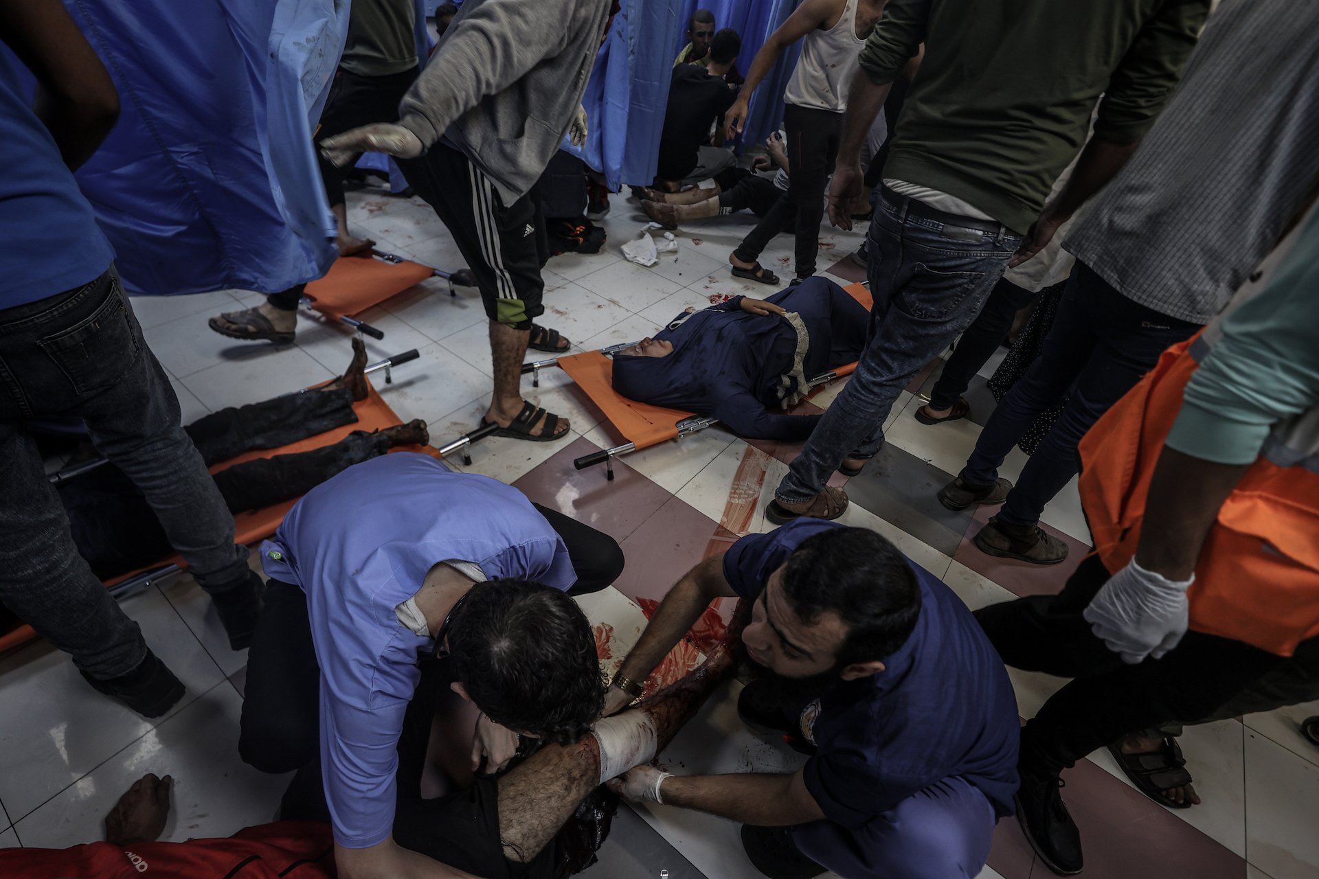 Wounded people lie on the floor while others care for them to the best of their ability without essential medical supplies or infrastructure.