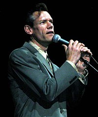 Singer Randy Travis, wearing a gray suit while singing into a microphone.