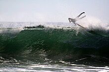 Photo of surfer catapulted into the air with feet higher than the head at 45-degree angle to the surface