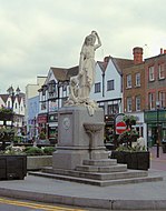 Statue on a plinth of a woman in classical dress carrying a jug on her shoulder and holding a child's hand. Steps up to the base of the plinth lead to a drinking fountain.