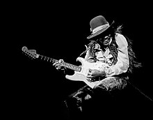 A black and white photograph of a man playing an electric guitar.