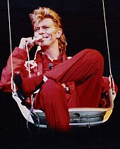 A man sitting on a high-wire chair holding a microphone