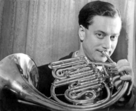 Young white man, clean-shaven, with groomed dark hair, holding french horn