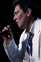 A woman wearing a white suit with her eyes closed, holding a microphone.